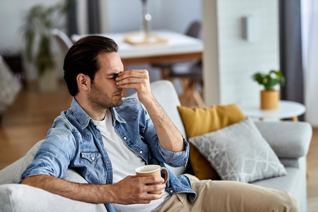 Young man holding his head in pain while sitting on the sofa at home