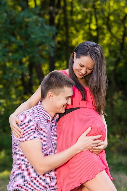 young man holding his pregnant wife in a park