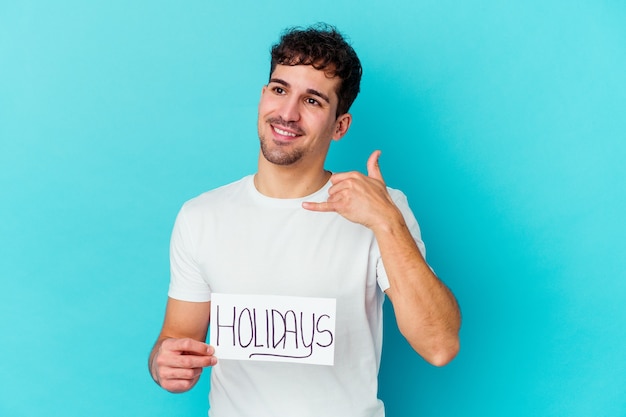 Young man holding a holidays placard isolated showing a mobile phone call gesture with fingers