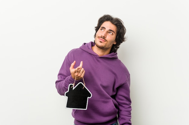 Young man holding a house icon shape dreaming of achieving goals and purposes