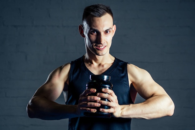 A young man holding a jar of protein in the gym