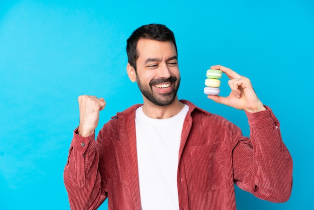 Young man holding macaroons over isolated wall