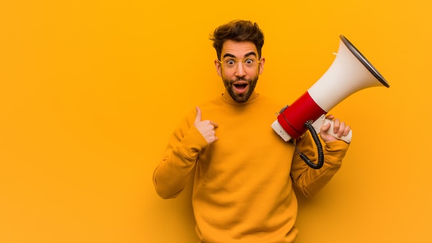 Young man holding a megaphone surprised, feels successful and prosperous