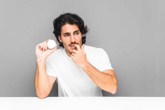 Young man holding a moisturizer relaxed thinking about something looking at a blank space.