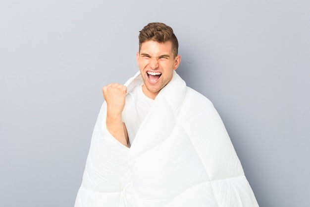 Young man holding a nordic duvet cheering carefree and excited. Victory concept.