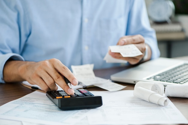 Photo young man holding pen working on calculator to calculate business data taxes bills payment