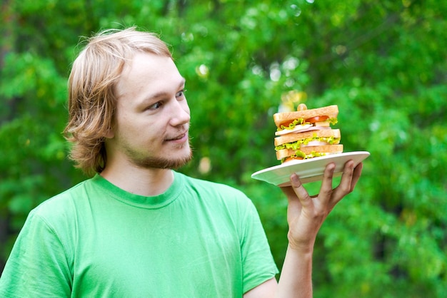 Young man holding piece big sausage sandwich on plate student eats fast food