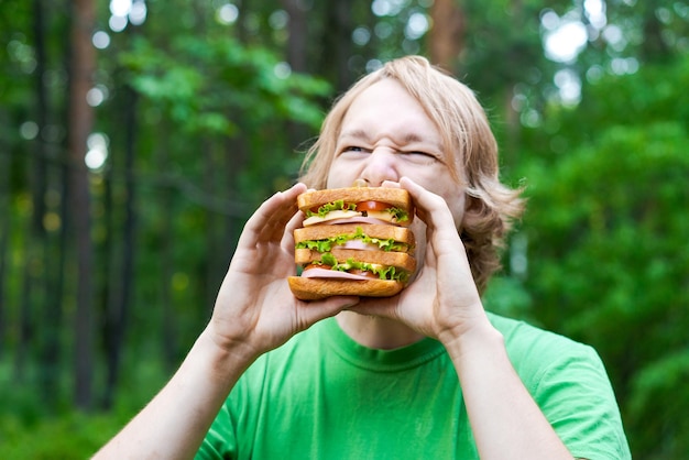 Young man holding piece big sausage sandwich on plate Student eats fast food