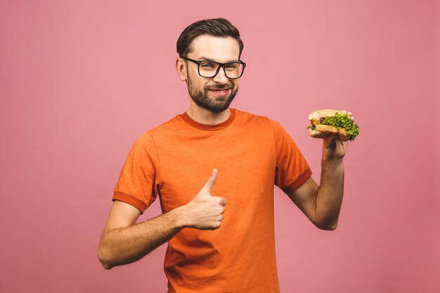 Young man holding a piece of hamburger. Student eats fast food. Very hungry guy. Thumbs up.