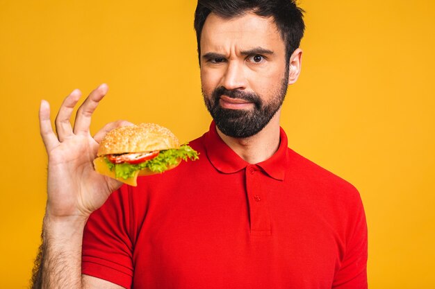 Young man holding a piece of sandwich. Student eats fast food. Burger is not helpful food.