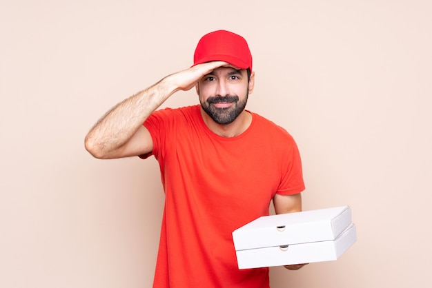 Young man holding a pizza over isolated  looking far away with hand to look something