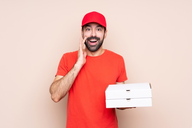 Young man holding a pizza over isolated wall with surprise and shocked facial expression