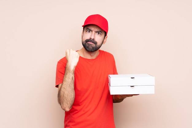 Молодой человек держит пиццу над изолированным с злым жестом