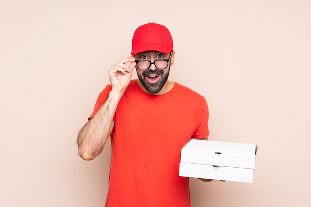 Young man holding a pizza over isolated  with glasses and surprised
