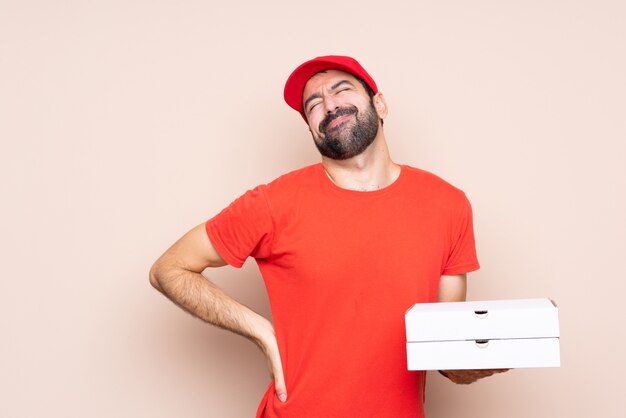 Young man holding a pizza suffering from backache for having made an effort