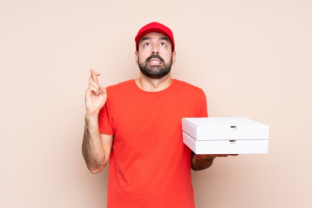 Young man holding a pizza with fingers crossing and wishing the best