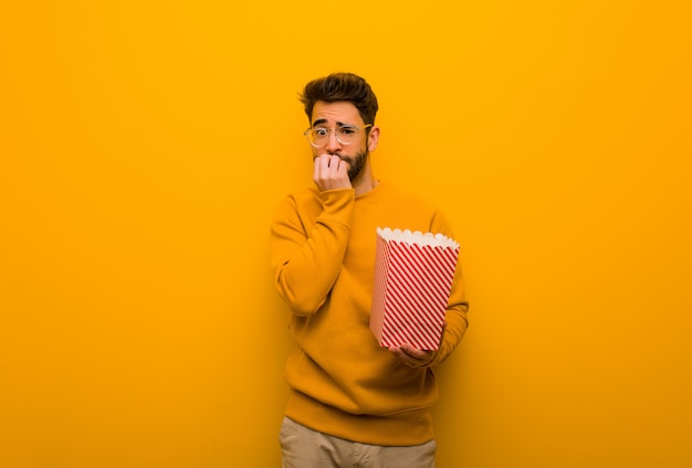 Young man holding popcorns biting nails, nervous and very anxious