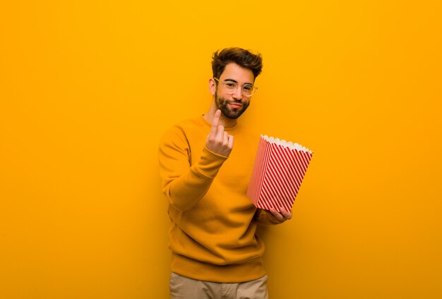 Young man holding popcorns inviting to come