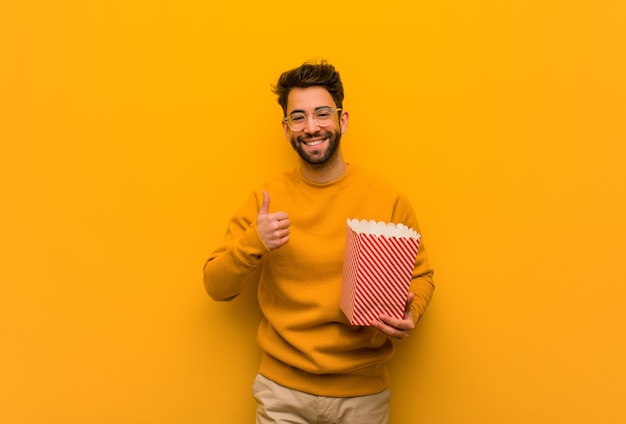 Young man holding popcorns smiling and raising thumb up