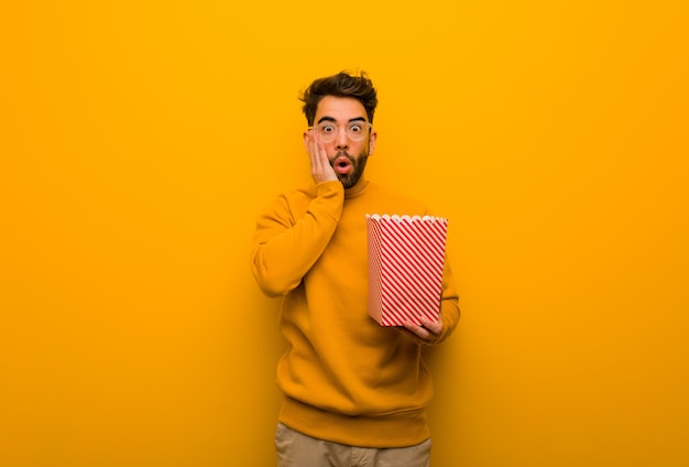 Young man holding popcorns surprised and shocked