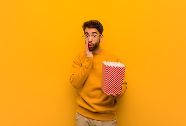 Young man holding popcorns whispering gossip undertone