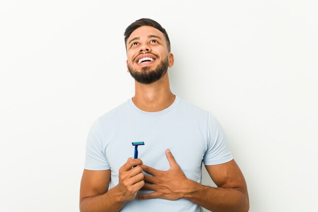 Young man holding a razor blade laughs out loudly keeping hand on chest