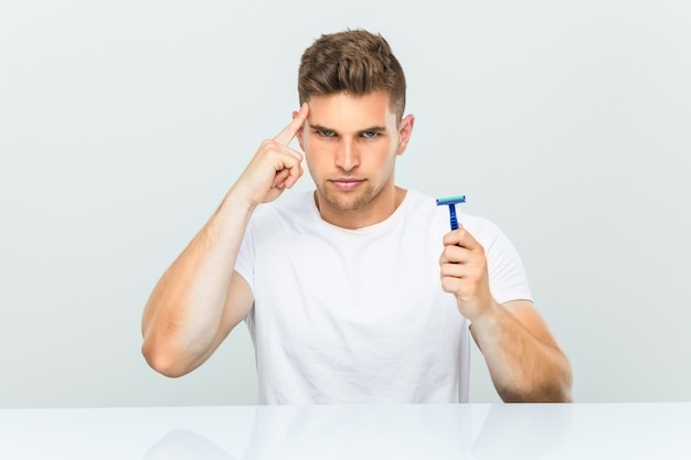 Young man holding a razor blade pointing his temple with finger