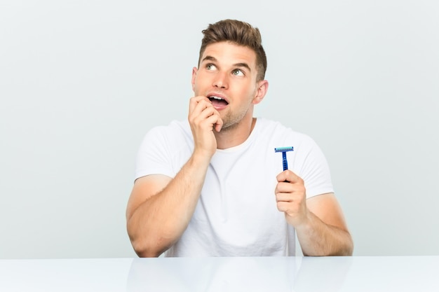 Young man holding a razor blade relaxed thinking about something looking at a copy space.