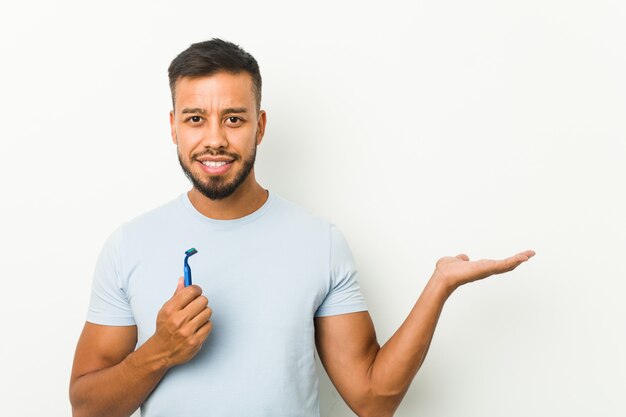 Young man holding a razor blade showing a blank space on a palm and holding a razor in the other hand