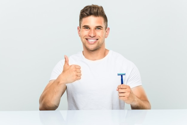 Young man holding a razor blade smiling and raising thumb up