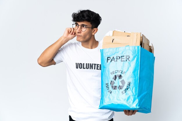 Young man holding a recycling bag full of paper frustrated and covering ears