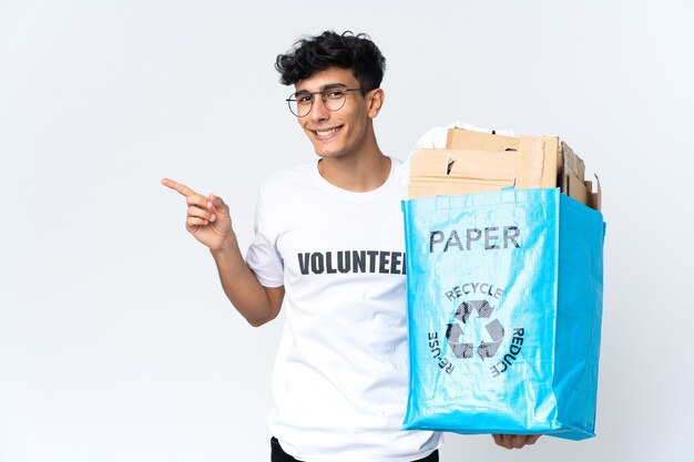 Young man holding a recycling bag full of paper pointing finger to the side