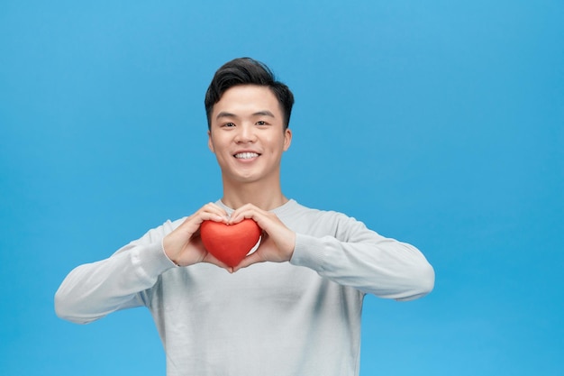 Young man holding red heart over blue background