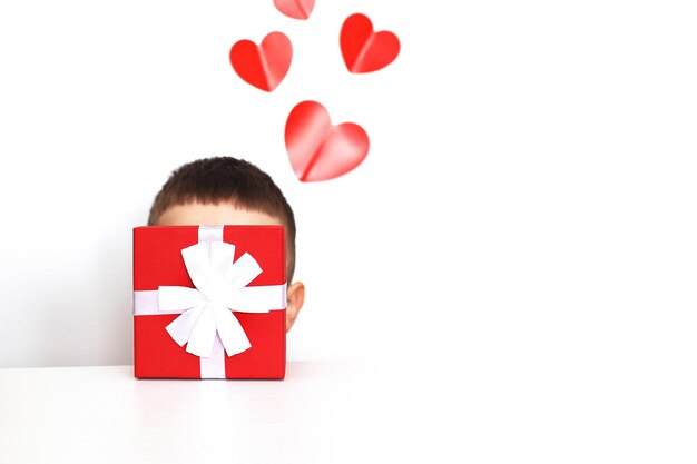 A young man holding a small present box with red hearts on a white background