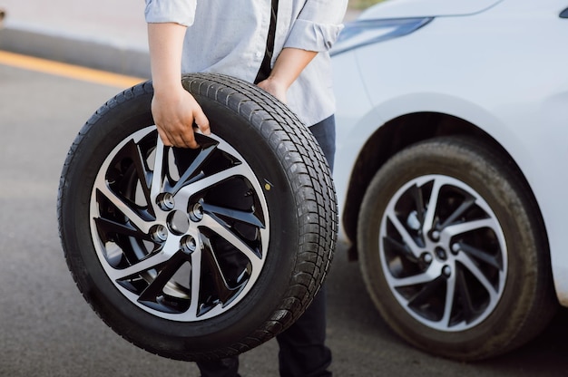 Young man holding spare wheel against for changing flat tire on the road