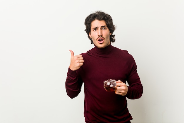 Young man holding a tea cup pointing to the side