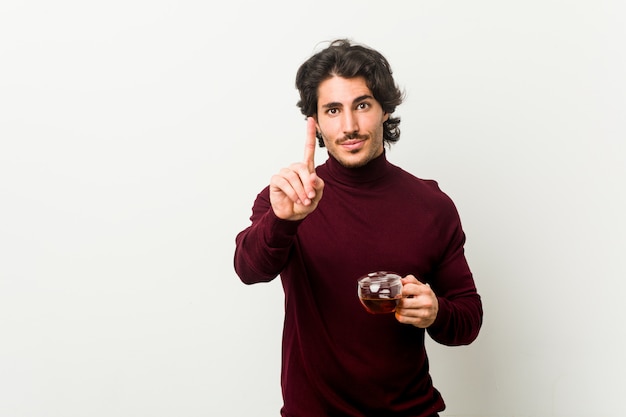 Young man holding a tea cup showing number one with finger.