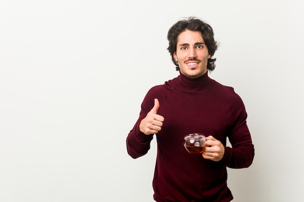 Young man holding a tea cup smiling and raising thumb up