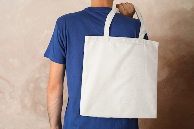 Young man holding tote bag against brown background