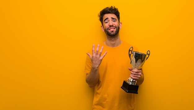 Young man holding a trophy very scared and afraid