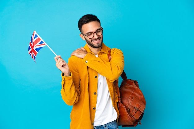 Young man holding an United Kingdom flag isolated on yellow wall suffering from pain in shoulder for having made an effort