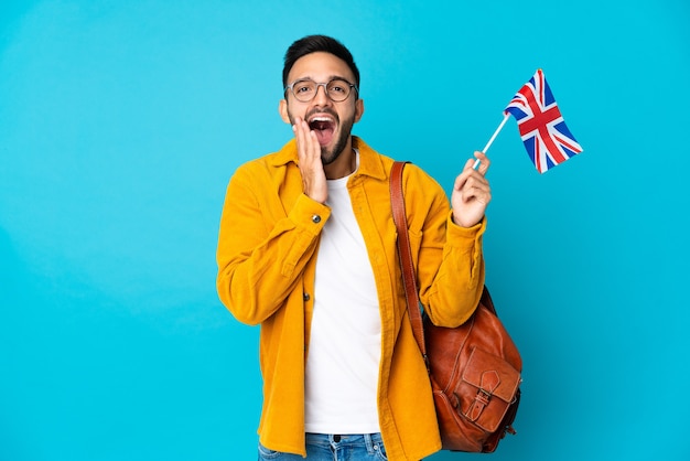 Young man holding an United Kingdom flag isolated on yellow wall with surprise and shocked facial expression