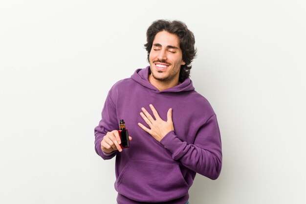 Young man holding a vaporizer laughs out loudly keeping hand on chest