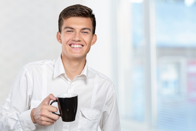 紅茶/コーヒーの暖かいカップを保持している若い男