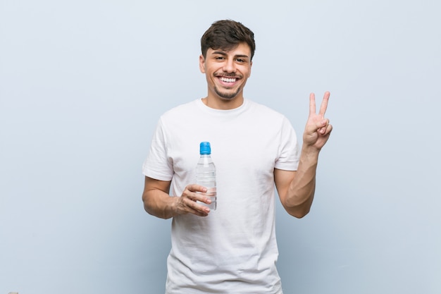 Young man holding a water bottle showing victory sign and smiling broadly
