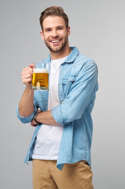 立っているビールのガラスを保持しているジーンズシャツを着て保持している若い男