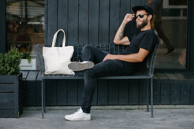 Молодой человек, держащий белую текстильную экологическую сумку на фоне городского города. . Концепция защиты экологии или окружающей среды. Белая эко-сумка для макета.