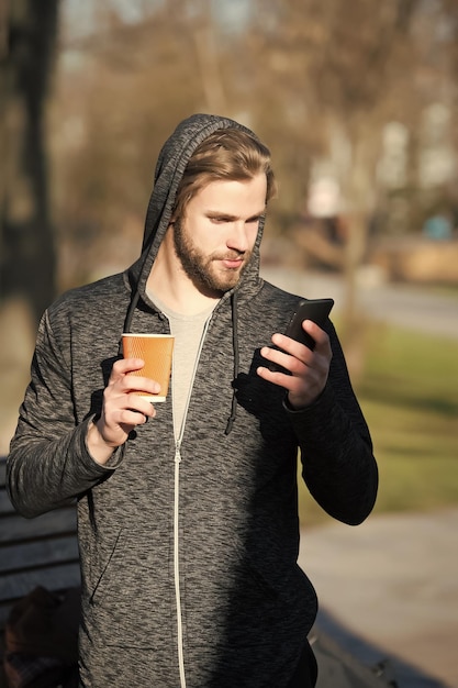 Молодой человек держит бумажный стаканчик кофе, чай, телефон в майке