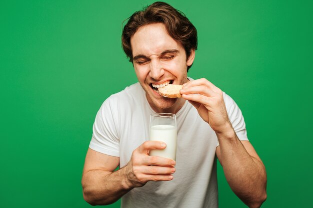 Young man holds glass of milk and bites cookie