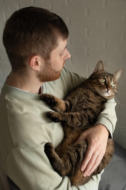Young man holds his cat in his arms vertical photo